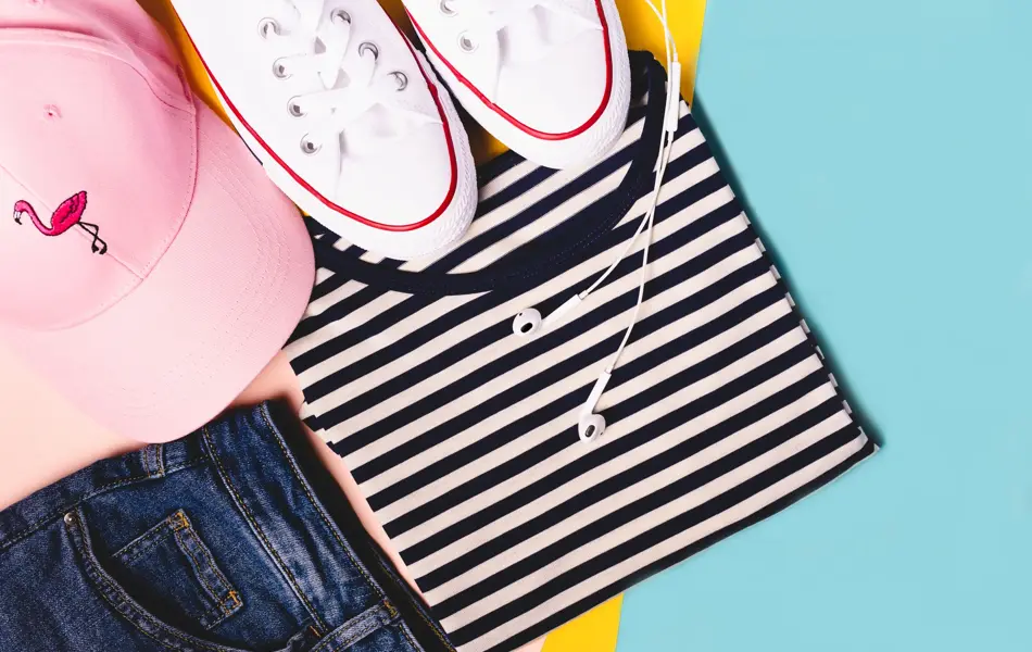 Fashion blogger concept. Summer sport, recreation and travel outfit: striped t-shirt, denim shorts, pink hat, white snickers. Minimal set of feminine teen clothes on pastel background