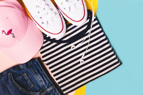 Fashion blogger concept. Summer sport, recreation and travel outfit: striped t-shirt, denim shorts, pink hat, white snickers. Minimal set of feminine teen clothes on pastel background