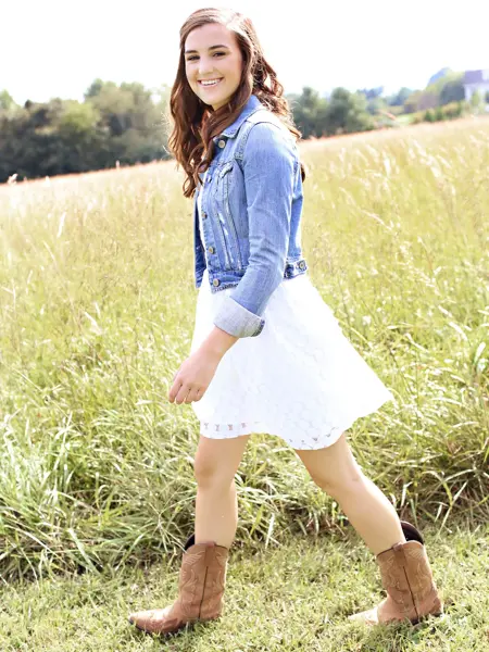 Dame med cowboyboots, sommerkjole og denimjakke går på en gresslette