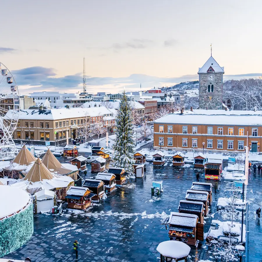 Julemarkedet på Torvet i Trondheim sett ovenfra, med pariserhjul, juletre, salgsboder og lavvoer i snødekt vinterlys.