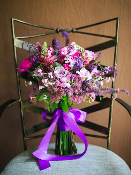 Bukett med rosa og lilla blomster med lilla sløyfe, plassert på en stol