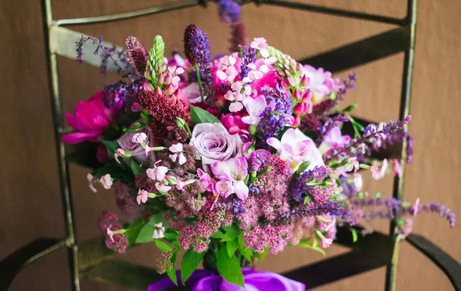Bukett med rosa og lilla blomster med lilla sløyfe, plassert på en stol