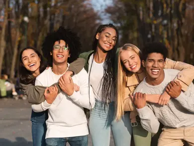 Positive group of multiracial young friends having fun at public park, hugging and smiling