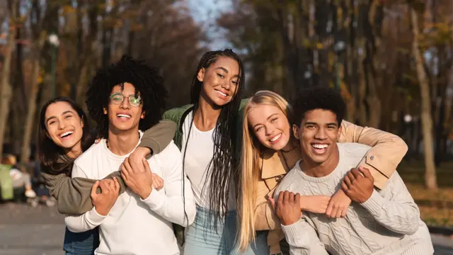 Positive group of multiracial young friends having fun at public park, hugging and smiling