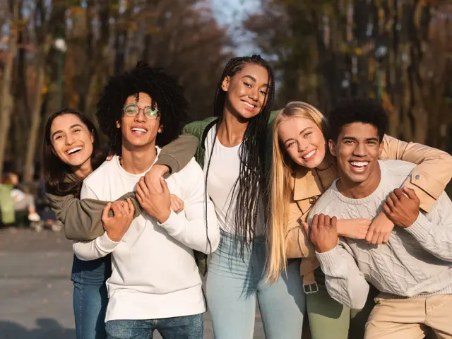 Positive group of multiracial young friends having fun at public park, hugging and smiling