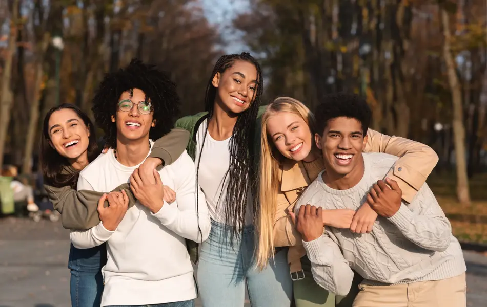 Positive group of multiracial young friends having fun at public park, hugging and smiling