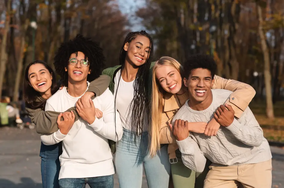 Positive group of multiracial young friends having fun at public park, hugging and smiling
