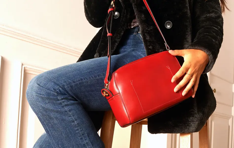 Halvportrett av dame som sitter på en krakk, med svart fløyelsjakke, jeans, rød veske og røde støvletter på seg.