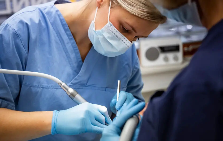 tannlege med munnbind, blå uniform og hansker som jobber med en kunde