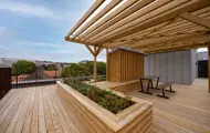 Delvis overbygd takterrasse med sitteplasser, plantekasser og utsikt mot byen.