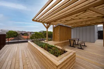 Delvis overbygd takterrasse med sitteplasser, plantekasser og utsikt mot byen.