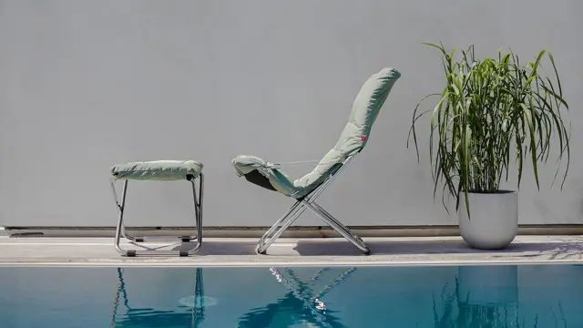 Grønn stol og krakk ved badebasseng og en grønn plante