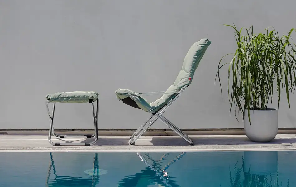 Grønn stol og krakk ved badebasseng og en grønn plante