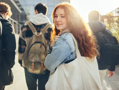 Female student glancing back while going for a class in college. Girl walking with friends going for class in high school.