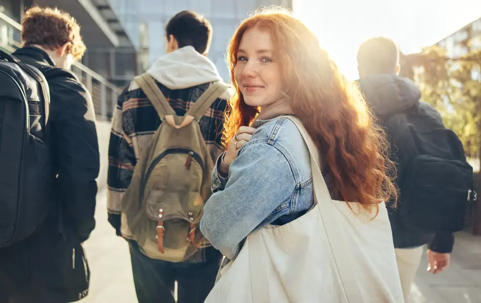 Female student glancing back while going for a class in college. Girl walking with friends going for class in high school.