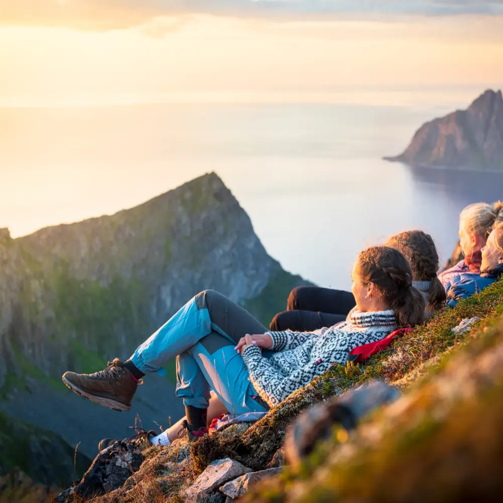 Friends relaxing together at sunset lying down on mountain ridge, Senja island, Troms county, Norway