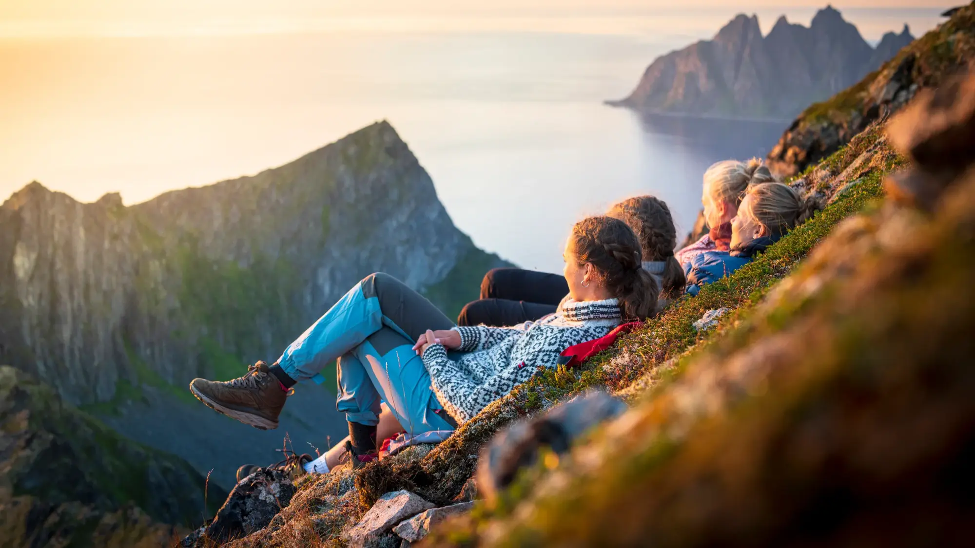 Friends relaxing together at sunset lying down on mountain ridge, Senja island, Troms county, Norway