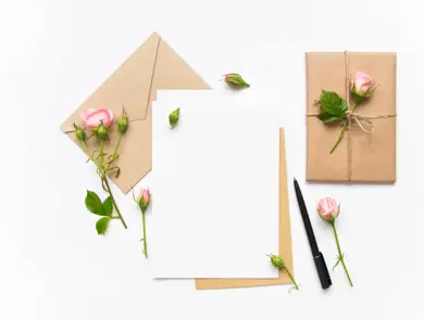 Letter, envelope and a present in eco paper on white background. Wedding invitation cards or love letter with pink roses. Valentine's day or other holiday concept, top view, flat lay, overhead view
