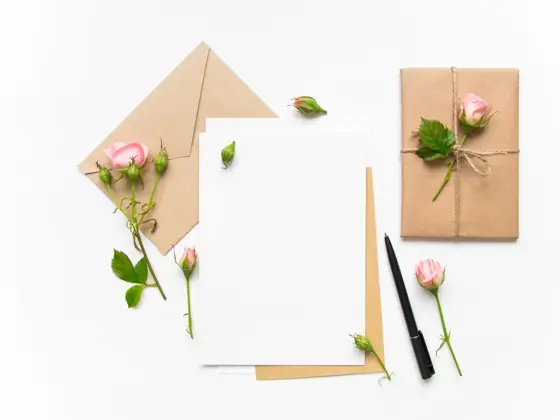 Letter, envelope and a present in eco paper on white background. Wedding invitation cards or love letter with pink roses. Valentine's day or other holiday concept, top view, flat lay, overhead view