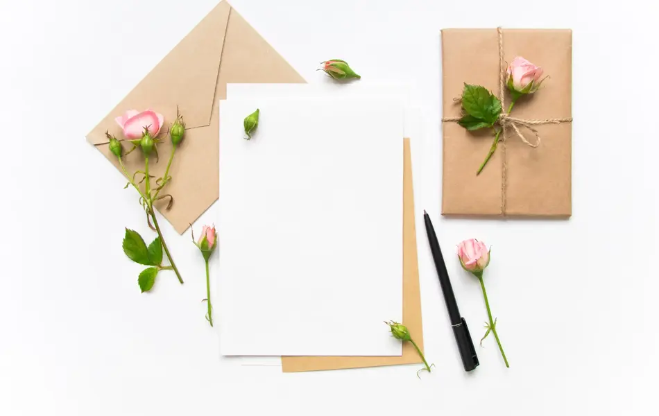 Letter, envelope and a present in eco paper on white background. Wedding invitation cards or love letter with pink roses. Valentine's day or other holiday concept, top view, flat lay, overhead view