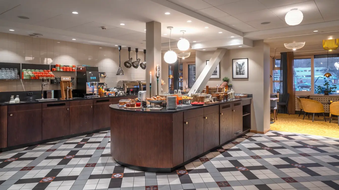 Frokostbuffé med bakevarer, syltetøy, frukt, frokostblanding, beholdere med varmmat.