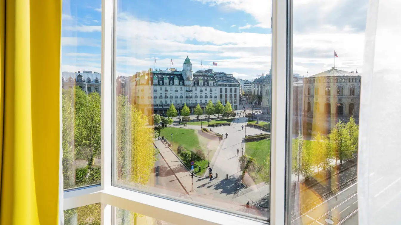 Gule gardiner og store vinduer med utsikt over Stortinget i junior suite på Thon Hotel Cecil