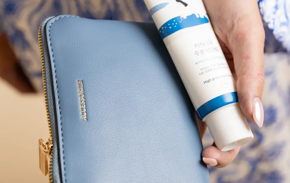 Hånd holder kremtube og blå lommebok.