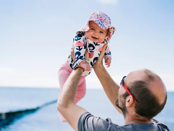 A father lifting his baby daughter in a sun bonnet up in the air,