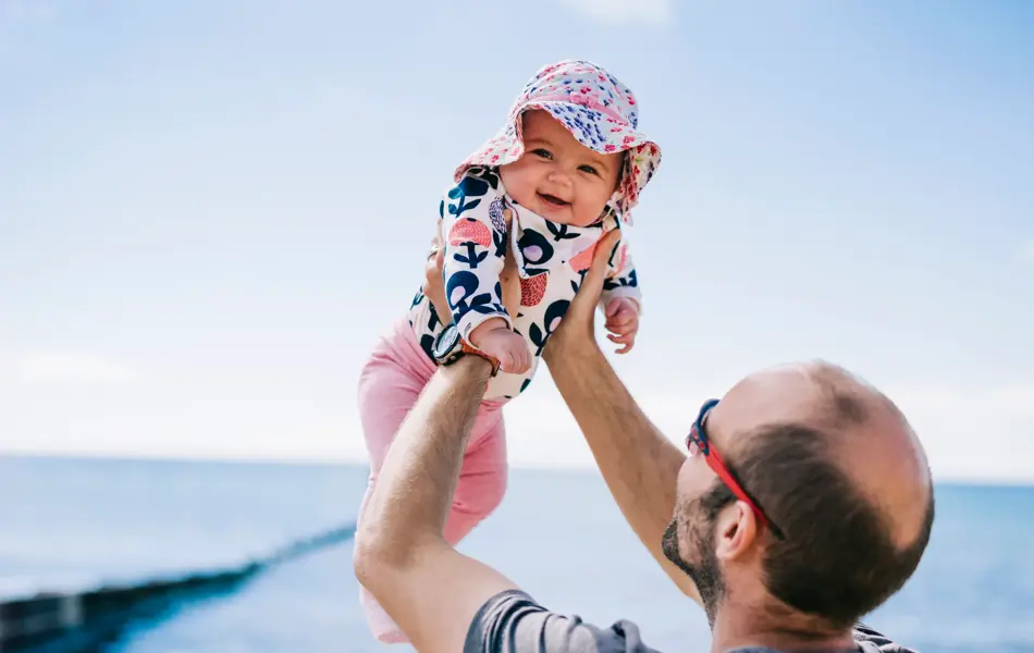 A father lifting his baby daughter in a sun bonnet up in the air,