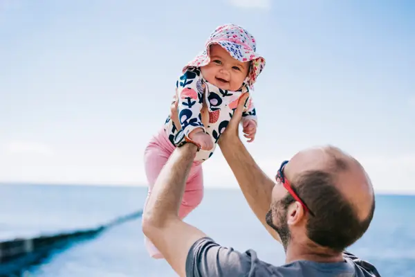 A father lifting his baby daughter in a sun bonnet up in the air,