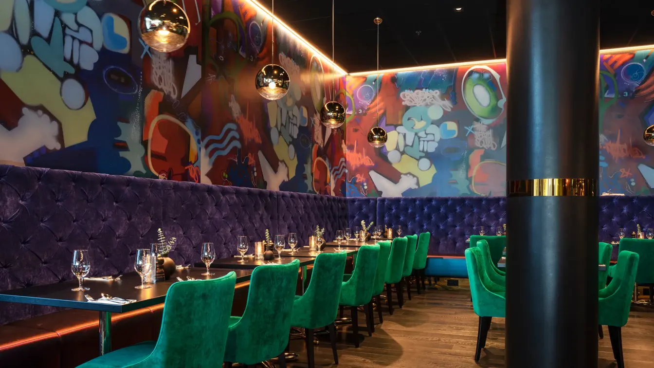 Vinglass på bord, blå sofa, grønne stoler og grafittitapet i restauranten på Thon Hotel Storo