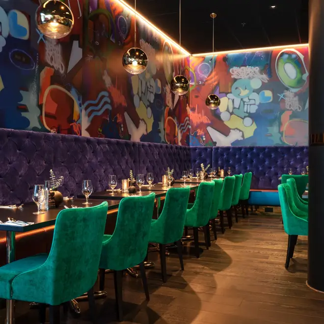 Vinglass på bord, blå sofa, grønne stoler og grafittitapet i restauranten på Thon Hotel Storo