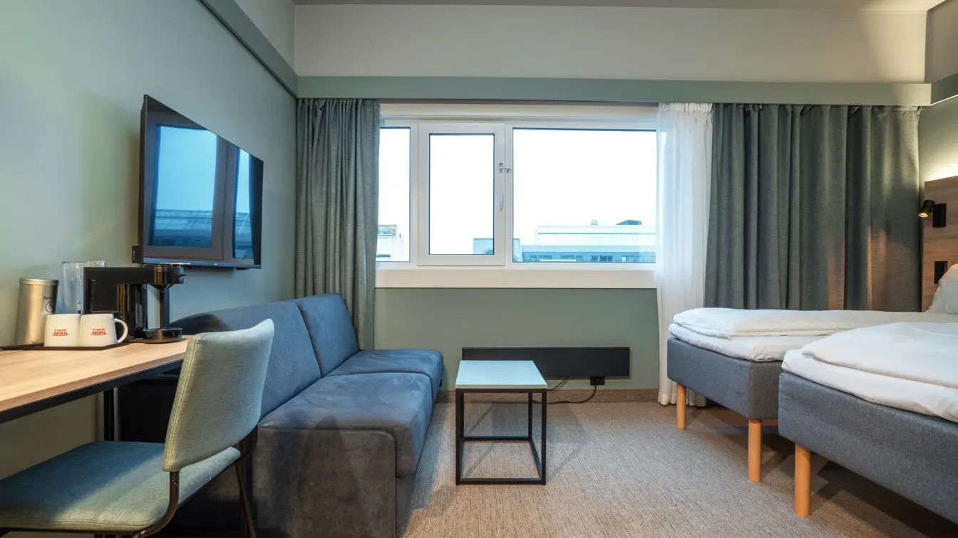 Sofa, TV, skrivebord og to enkeltsenger i Standard Twin Room hos Thon Partner Hotel Kristiansand.