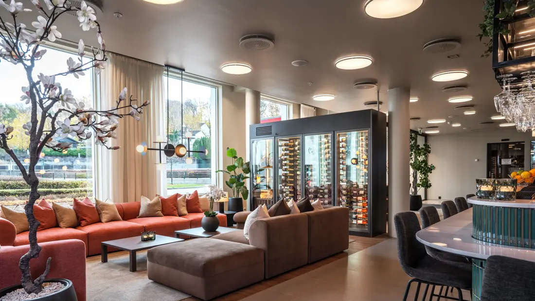 Lobbyområde med flere sittegrupper, resepsjonsdisk, stort vinskap og store vinduer