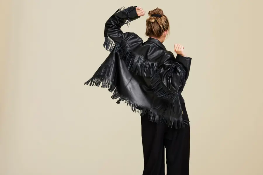 Et bilde av en kvinne i en frynsete skinnjakke som står med ryggen mot kameraet og danser