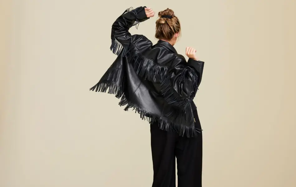 Et bilde av en kvinne i en frynsete skinnjakke som står med ryggen mot kameraet og danser
