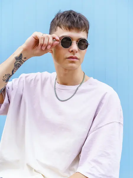 Ung mann med runde solbriller og hvit t-skjorte. 