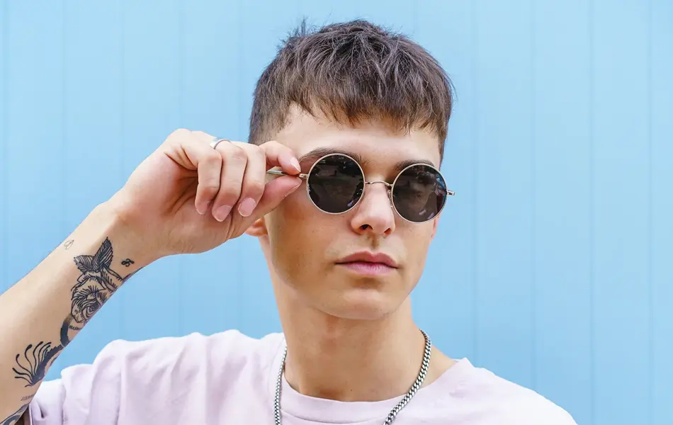 Ung mann med runde solbriller og hvit t-skjorte. 