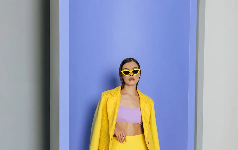 Modell med gul jakke og gult skjørt og lilla topp foran lilla vegg.