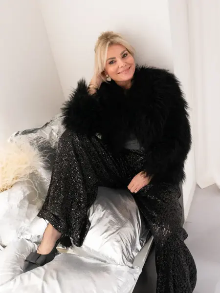 Dame med sort fuskepelsjakke, sølvtopp, glitrende bukser og pumps med sløyfe.