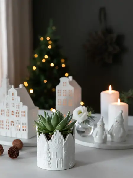Bord med lyslykter, potte med grønn plante, fat med kubbelys, liten vase med blomst og nissefigurer