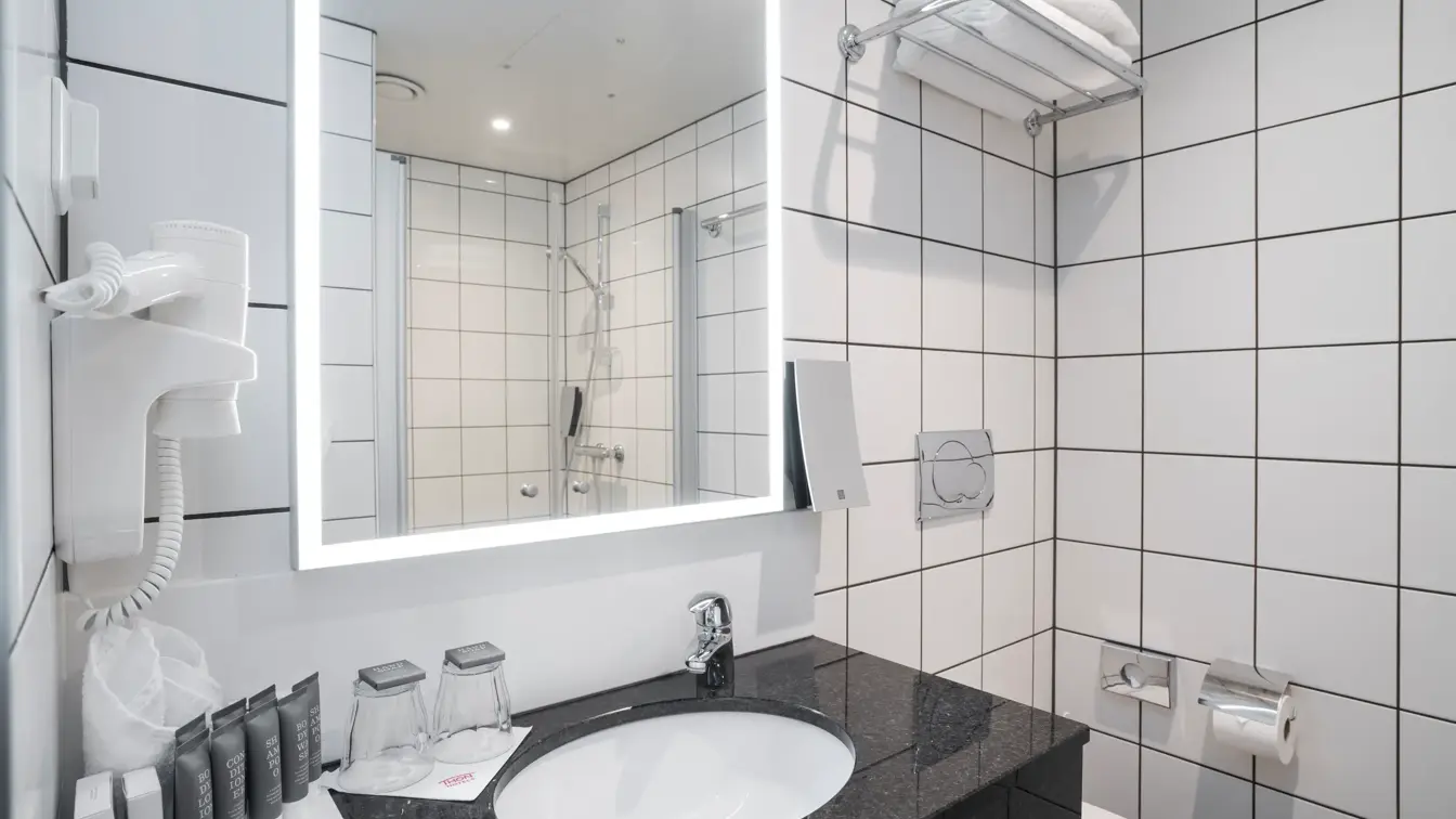 Servant i marmorbenk med toalettartikler og speil med led lys i bad på superior rom på Thon Hotel Kirkenes