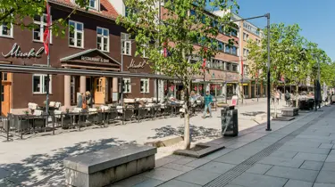 Bildet viser gågata i Lillestrøm med restauranter, butikker, grønne trer og benker.