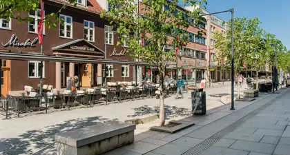Bildet viser gågata i Lillestrøm med restauranter, butikker, grønne trer og benker.