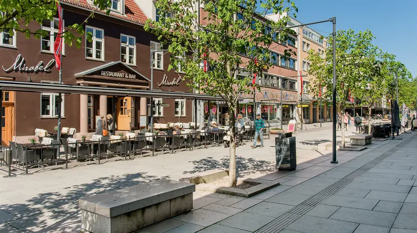 Bildet viser gågata i Lillestrøm med restauranter, butikker, grønne trer og benker.