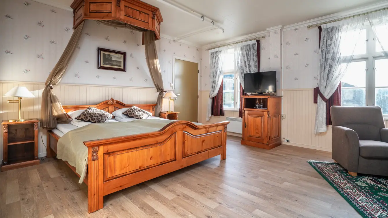 Dobbeltseng i mørkt tre med TV og sittegruppe på siden