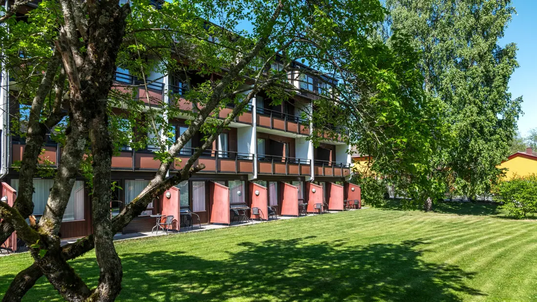 Deler av fasaden og et grønt uteområde med gressplen og trær