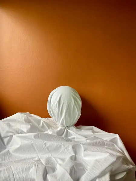 Oppblåst ballong inni et laken som ligger på et bord med oransje bakgrunn