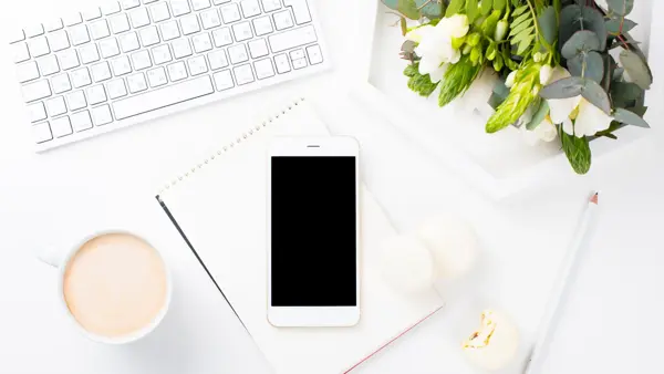 Telefon, tastatur og kaffekopp på et skrivebord