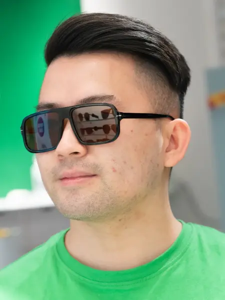 En gutt med mørkt kort hår som har på seg en grønn genser og sorte litt firkantede solbriller fra David Beckham